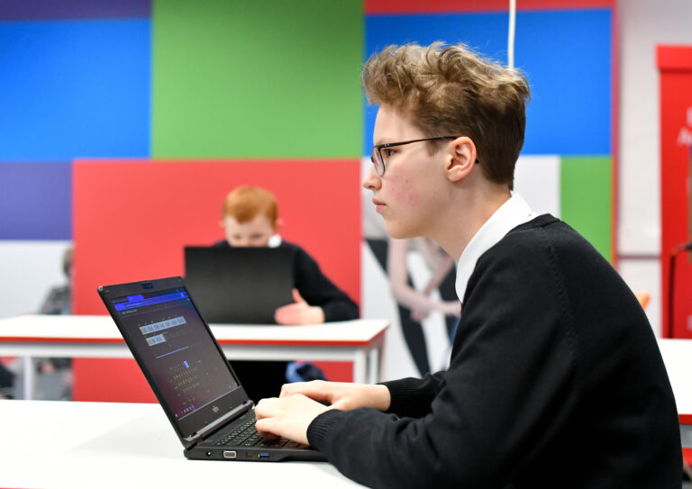 Side on view of student sat at a desk with a laptop, learning in a lesson