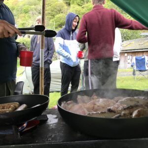 Bacon and sausages sizzling in the pan - students chatting in the background