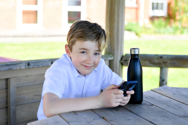 Male student using iPhone outside at lunchtime, smiling at the camera