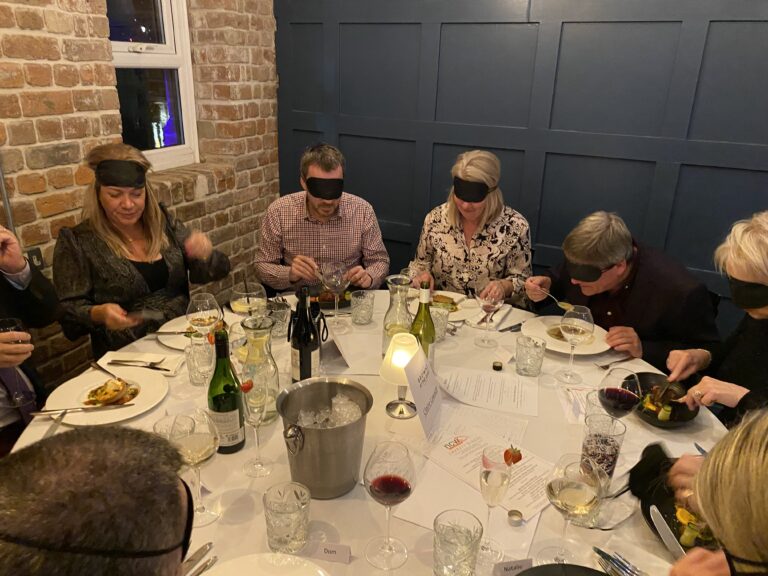 image of guests around a round table. some are blindfolded