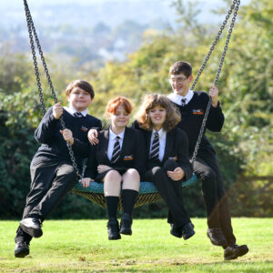 image of four students sat on a swing chatting and laughing