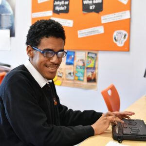 image of a student smiling in a lesson whilst reading a braille display