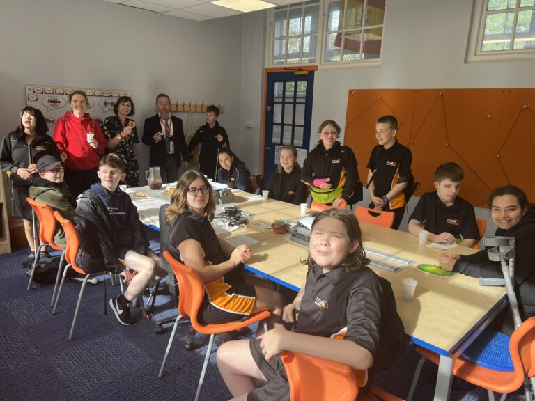 group photo of students and staff sat round a table enjoying treats