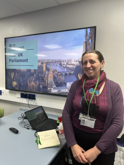 image of Clare smiling whilst stood next to a screen