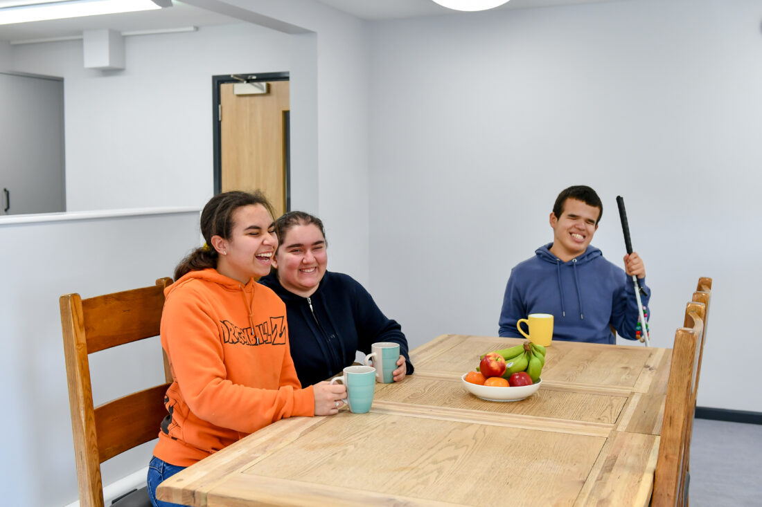 photo of three students sat at a table smiling whilst holding mugs