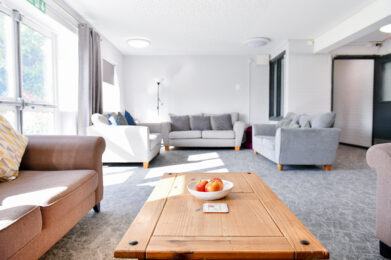 Photo of the seating area in the accommodation. There are large sofas in a neutral colour and grey carpets