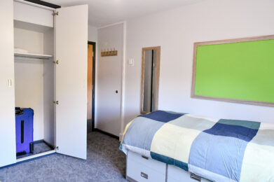 photo of a student's bedroom. There is a neatly made bed and a large wardrobe