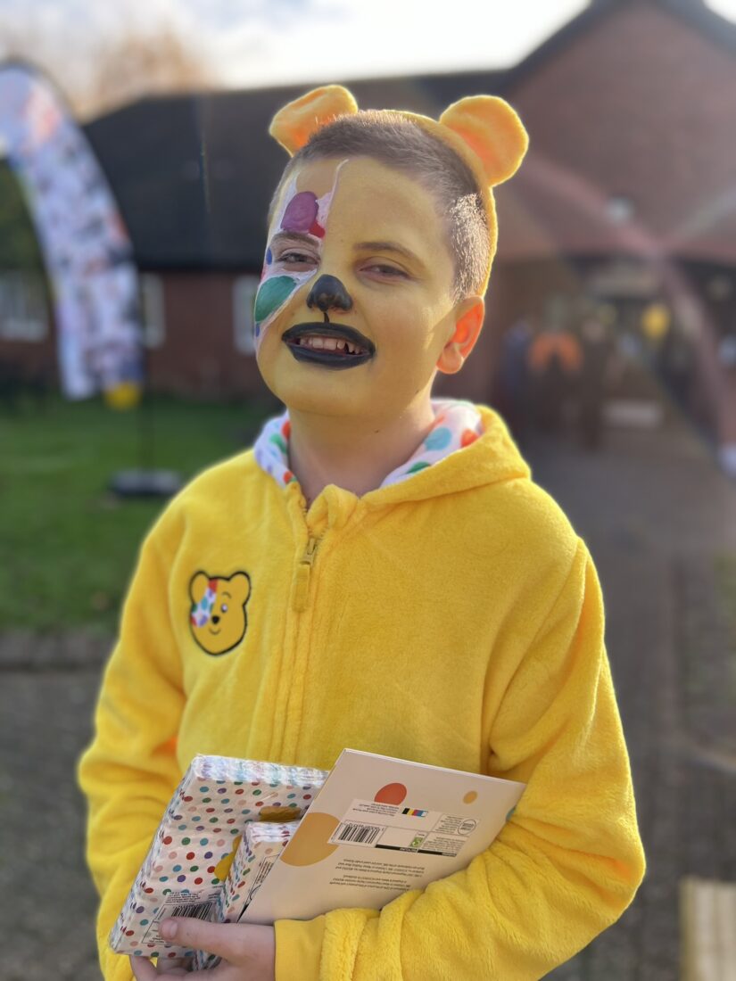 Image of a student dressed as Pudsey bear smiling at the camera. They also have their face painted like the bear with the classic eye patch