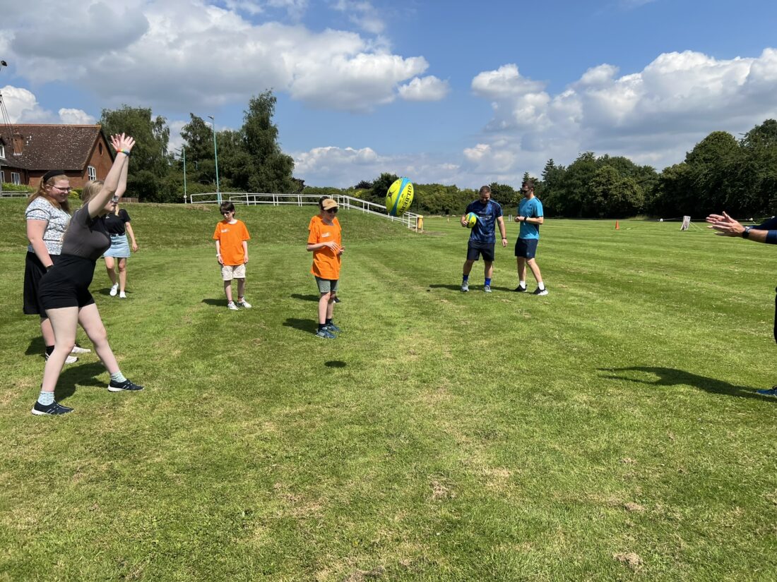 Image shows a group of young people throwing a rugby ball on a field