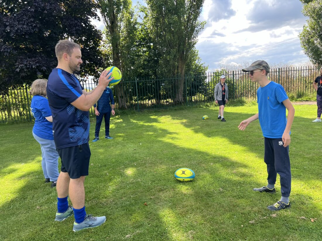 Image of a young person and member of staff playing rugby on a field