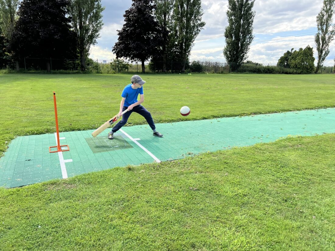 An image of a young person playing cricket on a field.