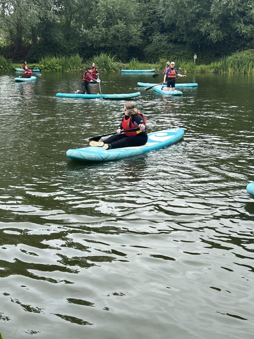 Image shows four people sat on paddleboards on a lake