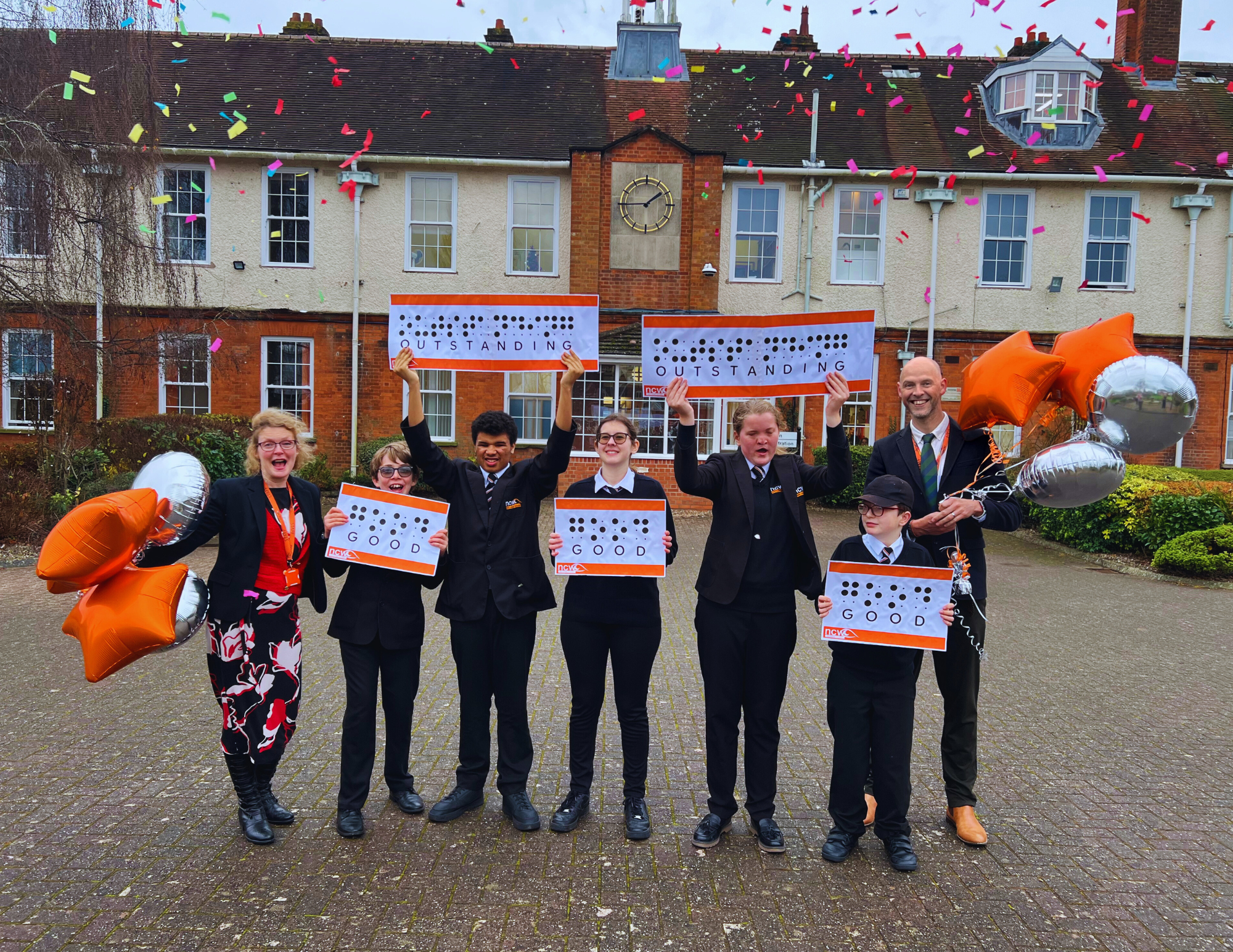 Students in front of school with Mrs Perks and Mr Farr, holding signs Good or Outstanding