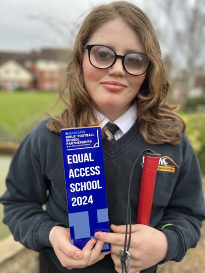 image of an NCW student with a vision impairment smiling at the camera whilst holding an award from Barclays "Equal Access School 24"